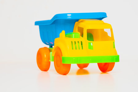 A colorful plastic toy truck with a yellow body and blue cargo area sits on a clean white surface, ready for children to enjoy their imaginative adventures and transport activities.の写真素材