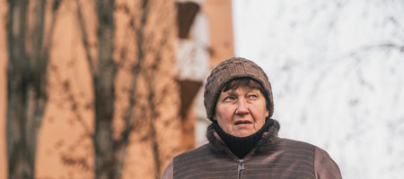 Elderly woman reflecting thoughtfully in urban park during a cool afternoon in early autumn.の写真素材