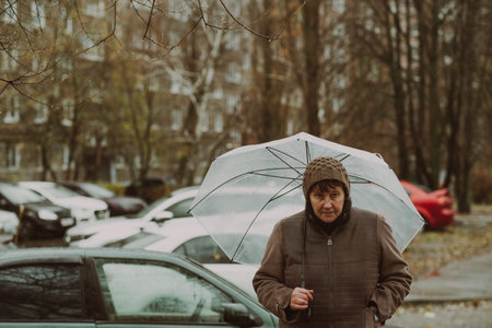 Thoughtful woman holding a transparent umbrella on a rainy day in an urban environment while contemplating life.の写真素材