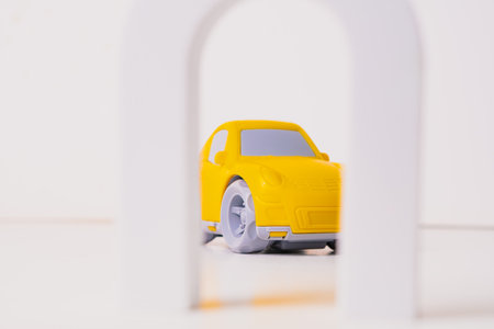 A bright yellow toy car is positioned behind a white arch. The colorful toy creates a sense of fun and encourages imaginative play in a simple, clean setting.の写真素材