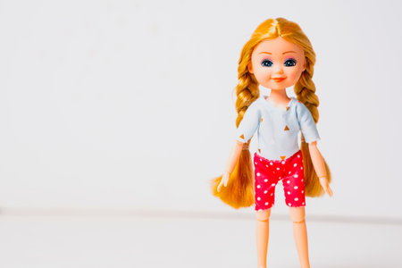 A cheerful toy doll with long blonde hair is dressed in a light blue top and red polka-dotted shorts. The doll stands upright, showcasing its vibrant appearance against a simple backdrop.の写真素材