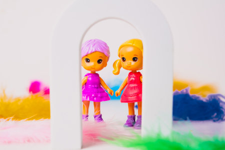 Two cheerful toy dolls stand hand in hand inside a small white arch, surrounded by colorful feathers. The dolls are dressed in bright outfits, creating a fun and playful scene.の写真素材