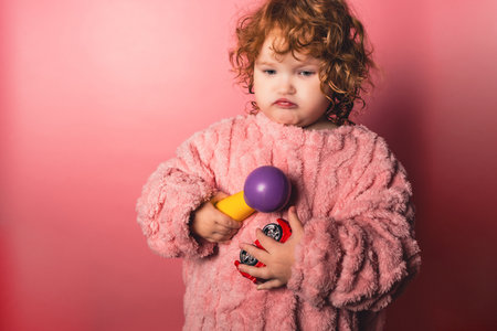 A child stands in a pink room clutching a purple toy while wearing a fuzzy sweater. The child appears to be engaged in play. The scene captures a moment of indoor activity.の写真素材