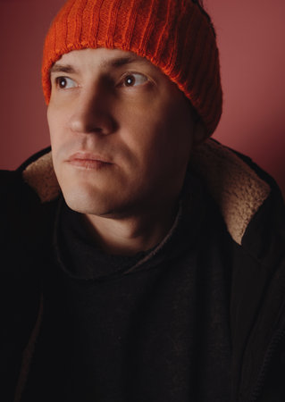 Man stands in front of a pink background wearing a black jacket and an orange headband indoors during the eveningの写真素材