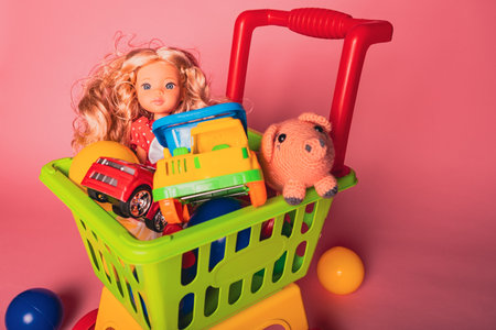 Colorful toy shopping cart with dolls, cars, and animals sitting on a pink background