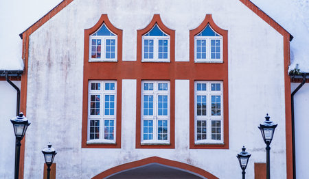 Building facade with snow on roof and street lamps. European architectural design, traditional house exterior in winter seasonの写真素材