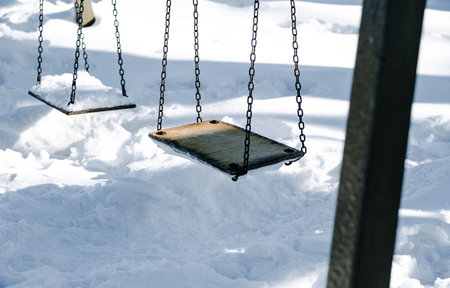Empty swing set covered in fresh white snow. Winter playground scene and seasonal outdoor activity concept. Cold weather landscapeの写真素材