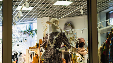 Mannequin woman dressed in a floral dress and hat in shop window display for fashion advertising. Clothing store interior with a reflectionの写真素材
