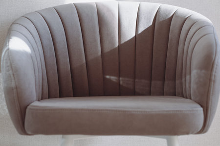 Beige upholstered armchair with vertical stitching. Elegant curved design, light-colored legs, soft play of light on fabricの写真素材