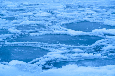 Close-up of icy surface with patches of snow and open water. Textured ice patterns, frosty edges,...