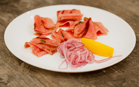 Tuna stroganina with lemon and onion slices on a white plate. Fresh raw fish dish for gourmet appetizerの写真素材