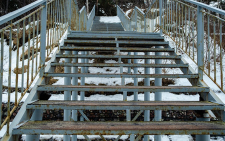 Old metal stairway with wooden steps leading up a snowy hill. Outdoor infrastructure element in winter nature. Rustic path conceptの写真素材