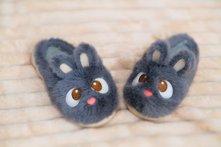 Gray rabbit house slippers for kid on pink furry blanket. Cute furry animal footwear, comfortable and soft. Gift ideaの写真素材