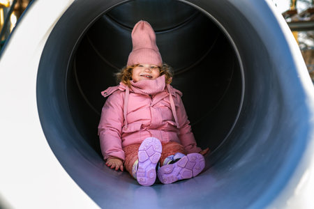 Young kid sitting inside a playground slide. Happy child playing outdoors during winter. Childhood...