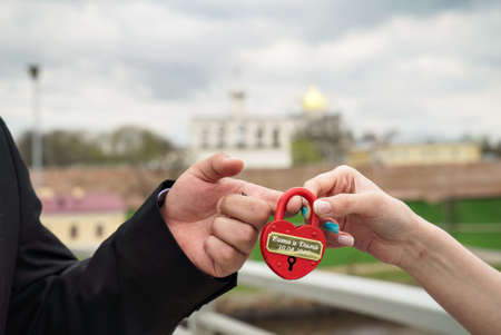 Red wedding lock in the hands of the bride and groom. Wedding theme, symbol of love, newlyweds. Kremlinの写真素材