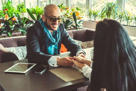 Arab man and the stylish girl sitting and holding hands in the restaurantの写真素材
