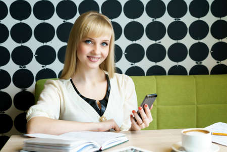 Blonde girl sitting in cafe holds a smartphoneの写真素材