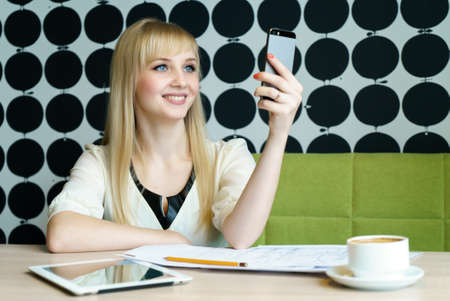Blonde girl sitting in cafe holds a smartphoneの写真素材