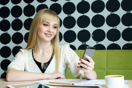 Blonde girl sitting in cafe holds a smartphoneの写真素材