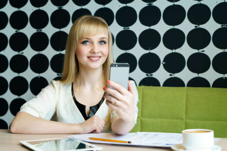 Blonde girl sitting in cafe holds a mobile phoneの写真素材