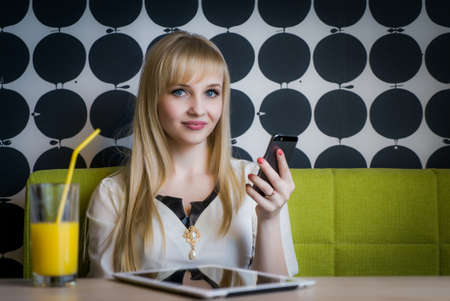 Young girl texting sms using a mobile phone and drinking orange juice at the cafeの写真素材
