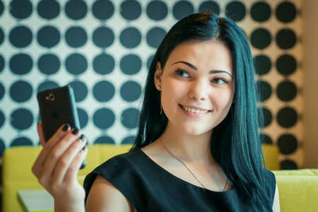 Young attractive model girl aged 20s making selfie photo using a smartphone indoorsの写真素材