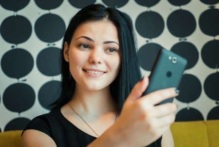 Young attractive model girl aged 20s making selfie photo using a smartphone indoorsの写真素材