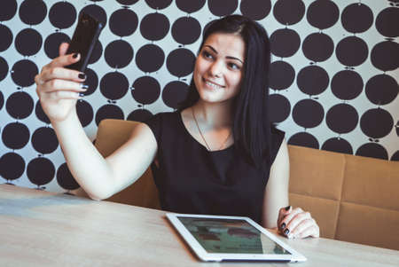 Brunette girl making selfie photo using a smartphone during coffee breakの写真素材