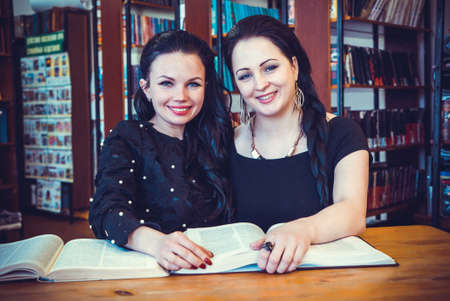 Two beautiful models women posing for camera at libraryの写真素材