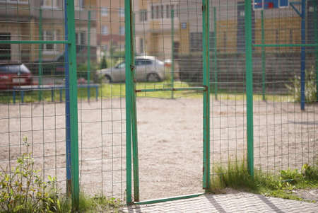 Broken steel mesh of metal fence of a basketball court in residential neighborhood in summerの写真素材