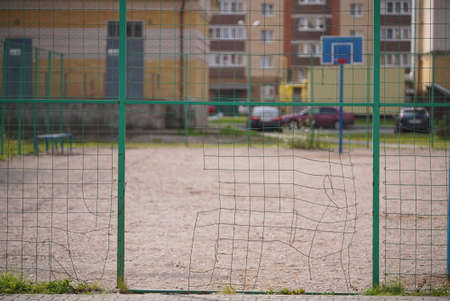 Broken steel mesh of metal fence of a basketball court in residential neighborhood in summerの写真素材