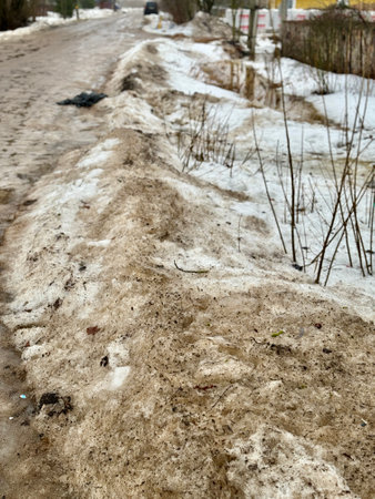 Melting dirty snow on the streets of the city in the daytime. Garbage in the snow.の写真素材