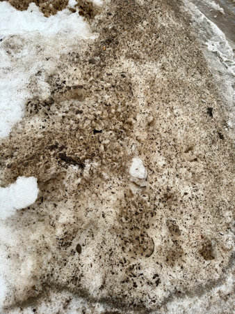 Melting dirty snow on the streets of the city during the daytime in winter. Snow with sand and mud lies on the roadの写真素材