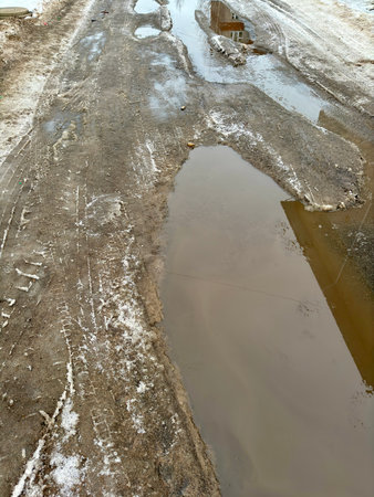 Melting dirty snow on the streets of the city during the daytime in winter. A big puddle on the road, a lot of dirty waterの写真素材