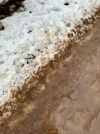 Melting dirty snow on the streets of the city during the daytime in winter. The pedestrian road is snow with sand and mud. Traces of people and petsの写真素材