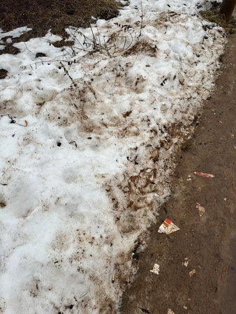 Melting dirty snow on the streets of the city during the daytime in winter. Snow with sand and mud lies on the roadの写真素材
