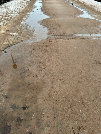 Melting dirty snow on the streets of the city during the daytime in winter. The pedestrian road is snow with sand and mud. Traces of people and petsの写真素材