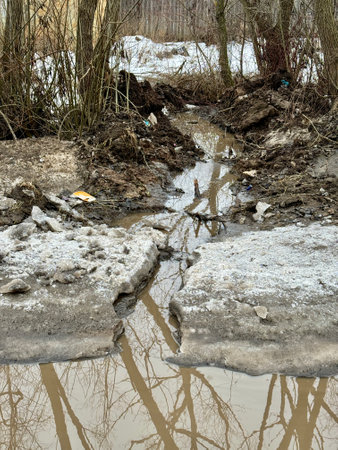 Melting dirty snow on the streets of the city during the daytime in winter. A big puddle on the road, a lot of dirty waterの写真素材