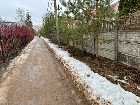 Melting dirty snow on the streets of the city during the daytime in winter. The pedestrian road along the fence has snow with sand and mud. Traces of people and petsの写真素材