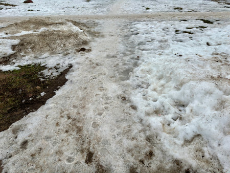 Melting dirty snow on the streets of the city during the daytime in winter. The pedestrian road is snow with sand and mud. Traces of people and petsの写真素材