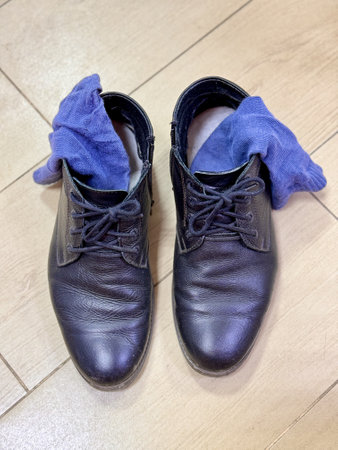 Old and dirty black lace-up shoes with blue socks inside are on ceramic tiles in the hallway of the houseの写真素材