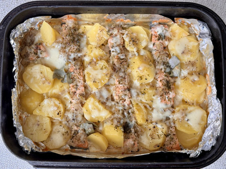 Baked salmon fish steaks with potatoes under mayonnaise lie on baking paper on a black baking sheet. Delicious fast food baked in the ovenの写真素材