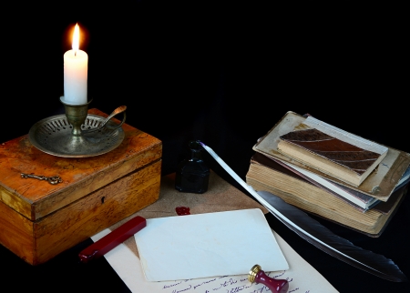 still life with a letter, a pen, a lighted candle in copper candlestick and a pile of old books on a dark backgroundの写真素材