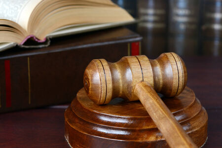 Wood gavel, soundblock and open book on the background of shelves of old books
