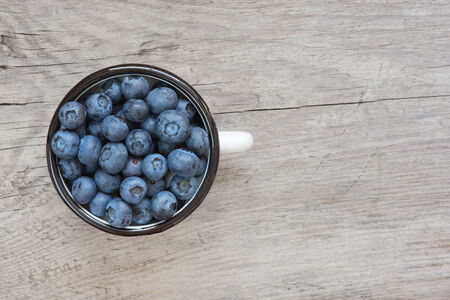 Blueberries in the old enamel mug on a wooden boardの写真素材