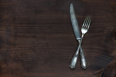 Crossed vintage fork and knife on old wooden board