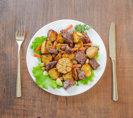 Roast with vegetables in a white plate on a wooden tableの写真素材