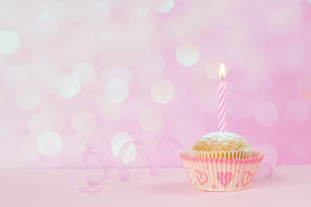 Small cupcakes with a one burning striped candle on a pink backgroundの写真素材
