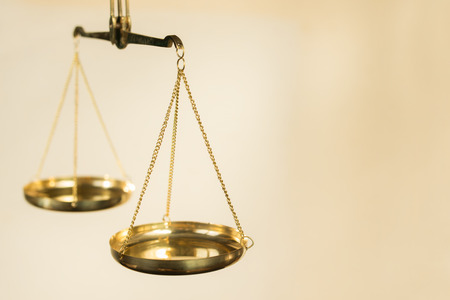 Two bowls of scales made of golden metal suspended on chains on a beige backgroundの写真素材