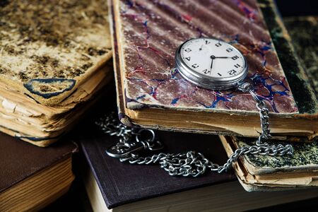 Vintage pocket watch with a steel chain lie on a pile of old booksの写真素材